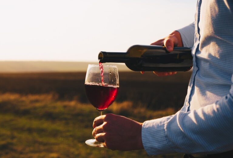 Personne qui verse du vin rouge dans un verre au coucher du soleil